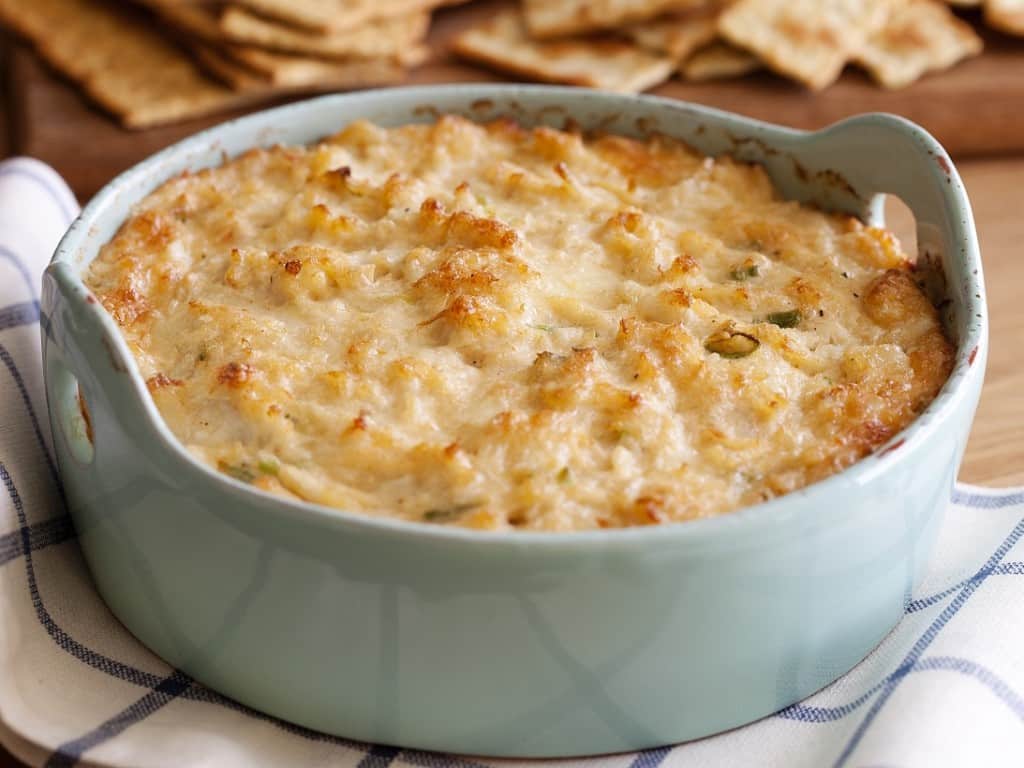 A bowl of cheesy dip with crackers on the side.